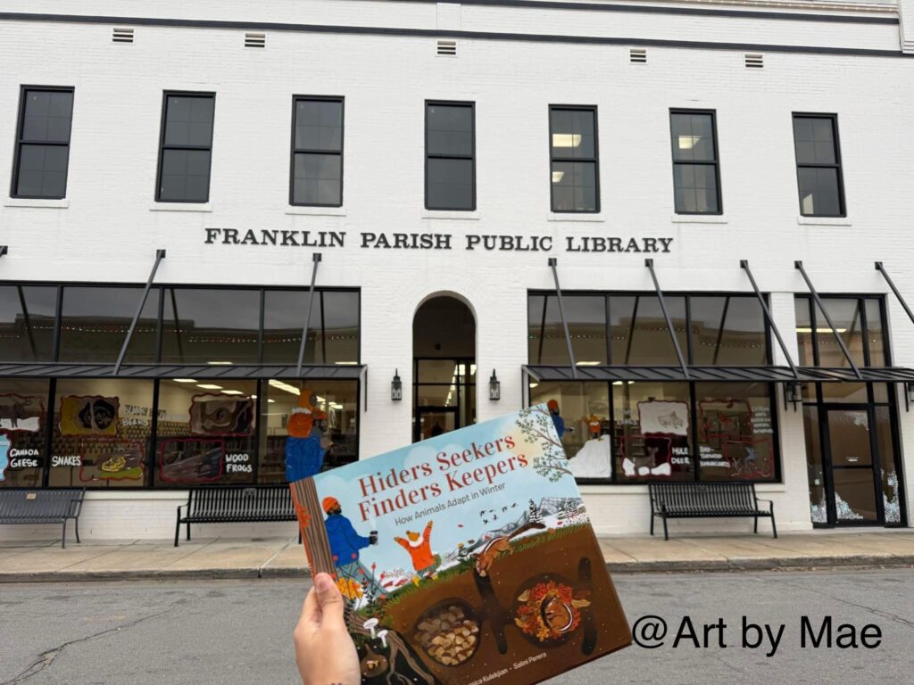 Photo of the front of the library with art painted on the library windows to match the winter story walk 2025. Art by Laisam Wallace